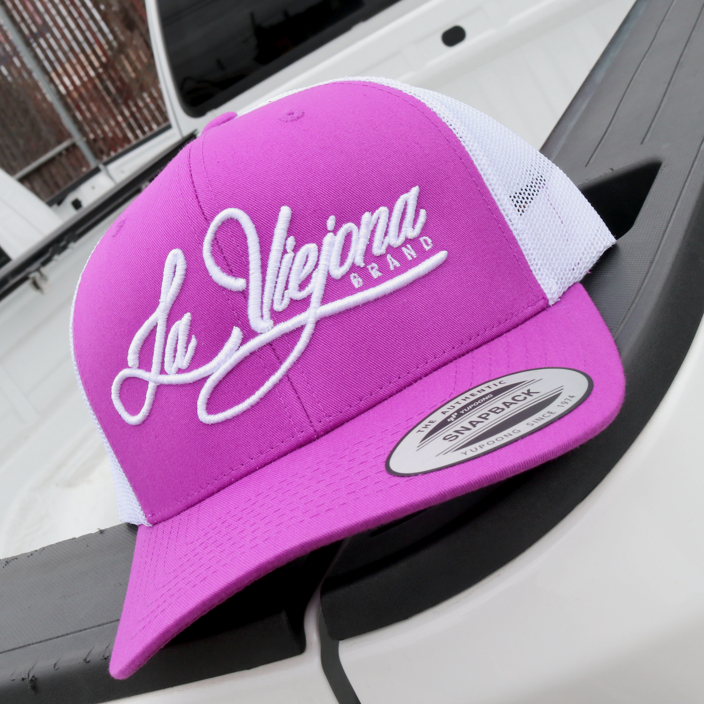 La Viejona magenta and white Yupoong Classic trucker hat with white embroidered script logo.