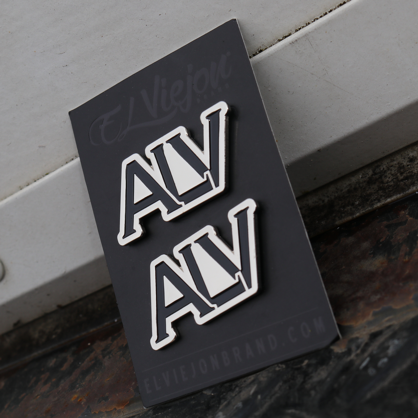 Two ALV brand pins, silver and black, on a black backing card.