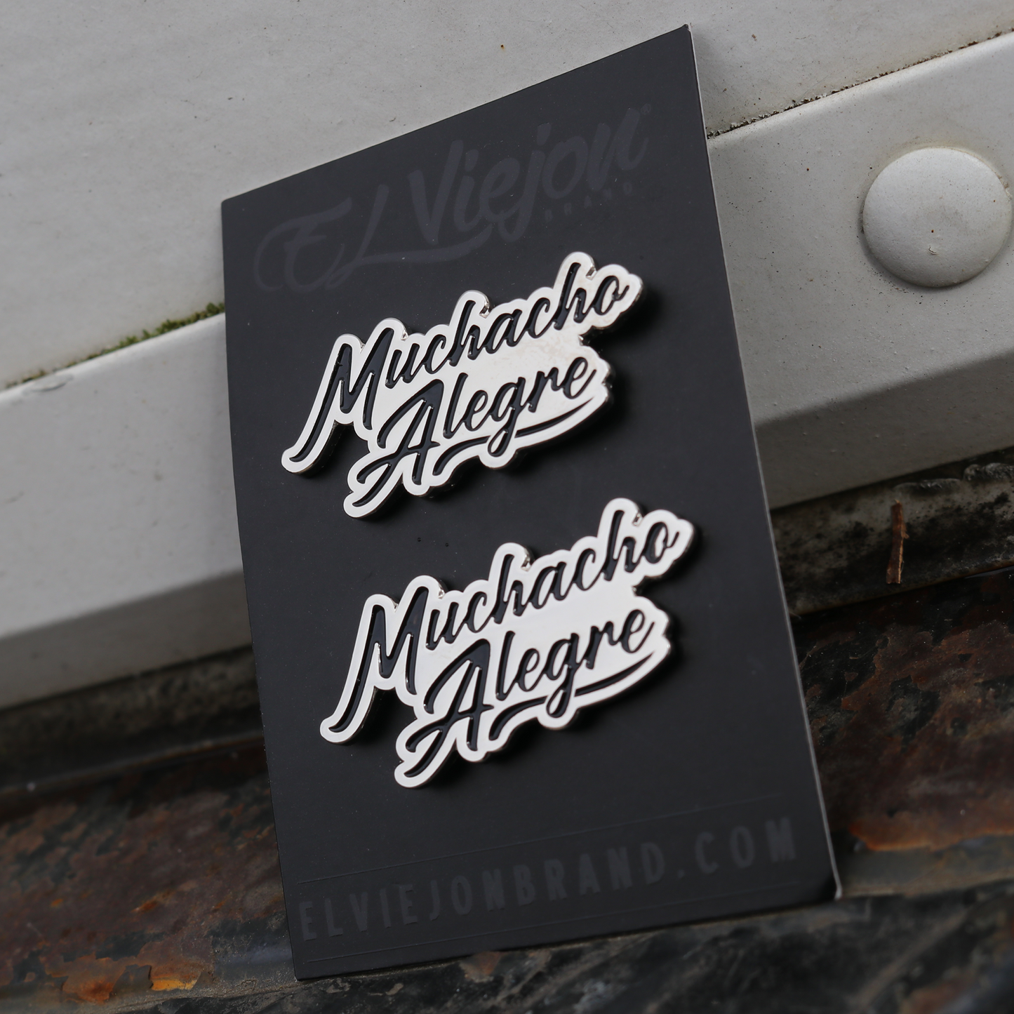 Two silver "Muchacho Alegre" script pins on a black El Viejon Brand card.