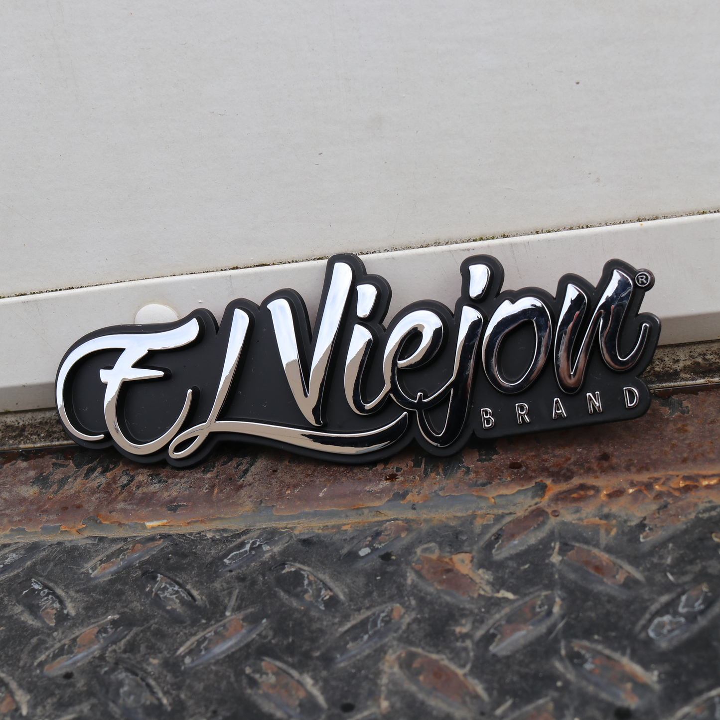 El Viejon Brand car emblem, 6.5" x 2.2" black ABS plastic with raised chrome script and "BRAND" text.
