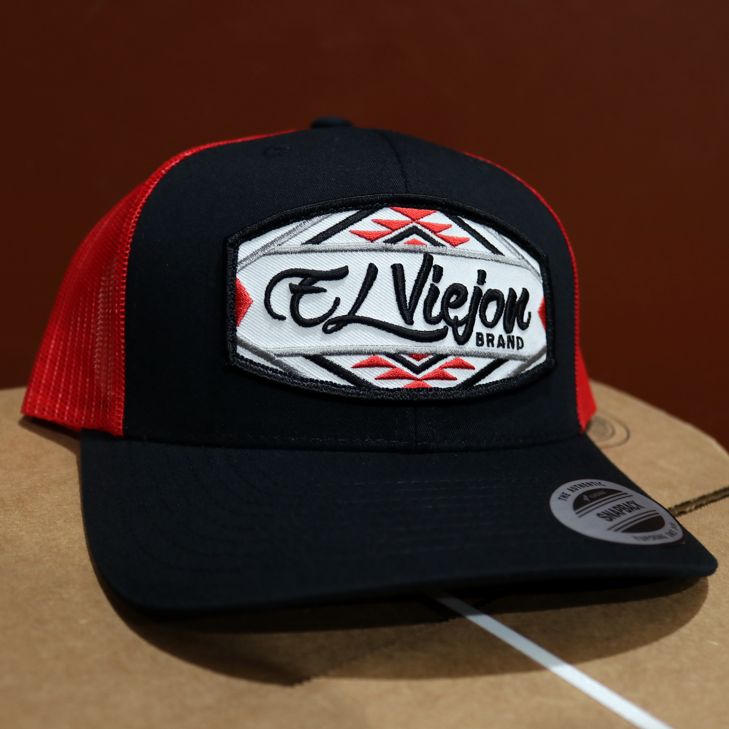 Black and red mesh trucker hat with "El Viejon Brand" Navajo-style embroidered patch.