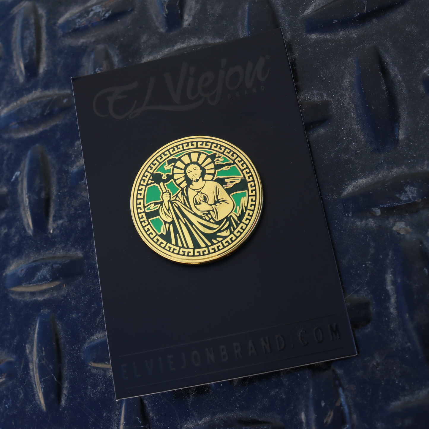 Gold and green San Judas pin with intricate design on black El Viejon Brand card.