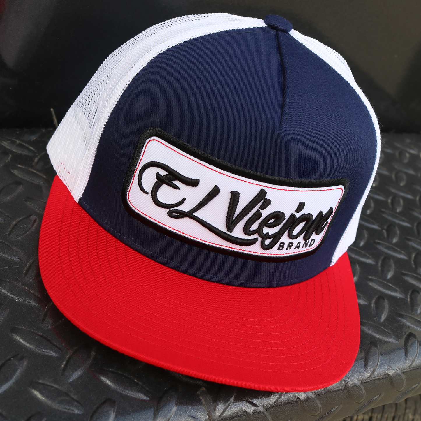 EVPatch Red/Navy/White flat visor trucker hat with "El Viejo Brand" patch, white mesh back.