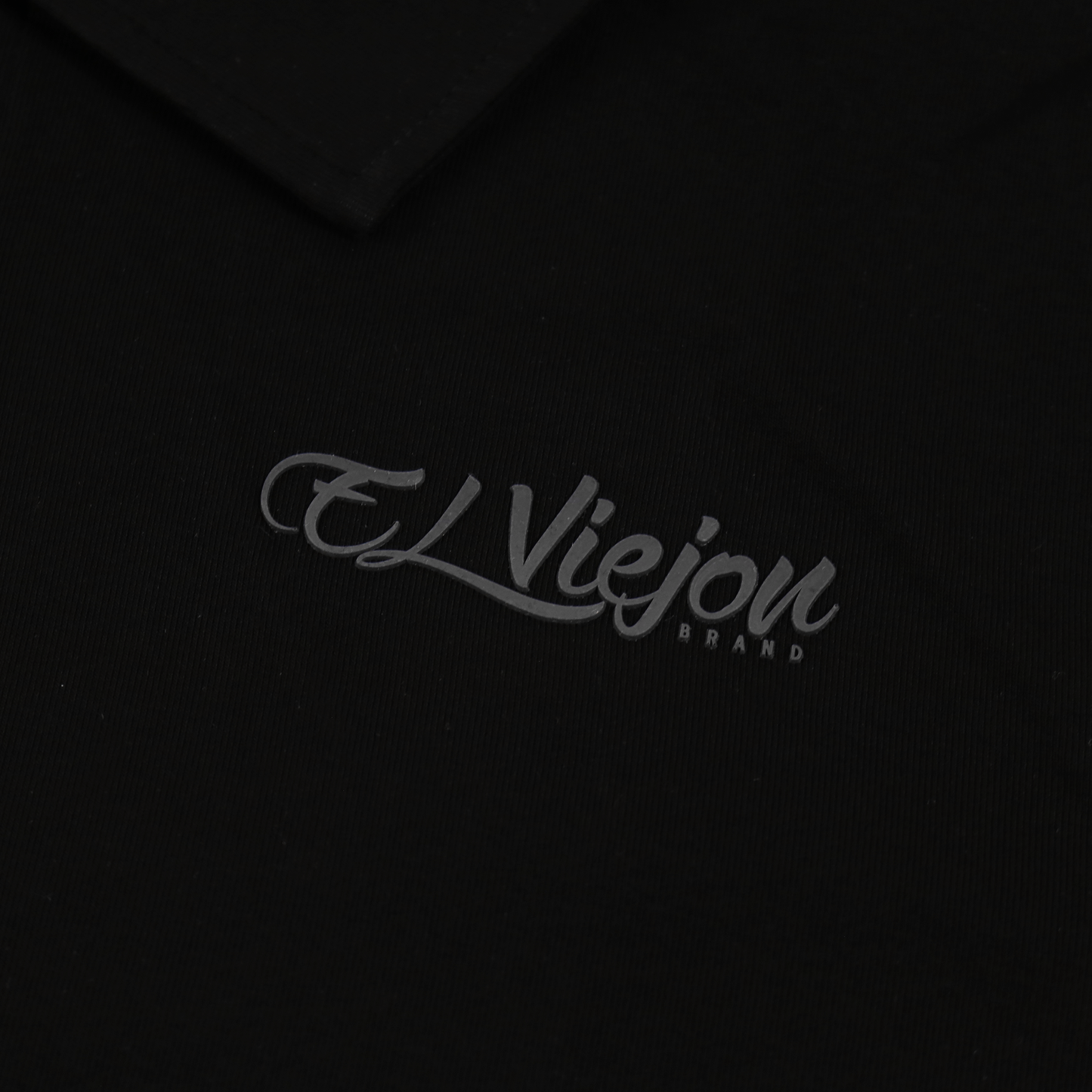 Black polo shirt with a subtle charcoal 3D vinyl "El Viejon Brand" logo.