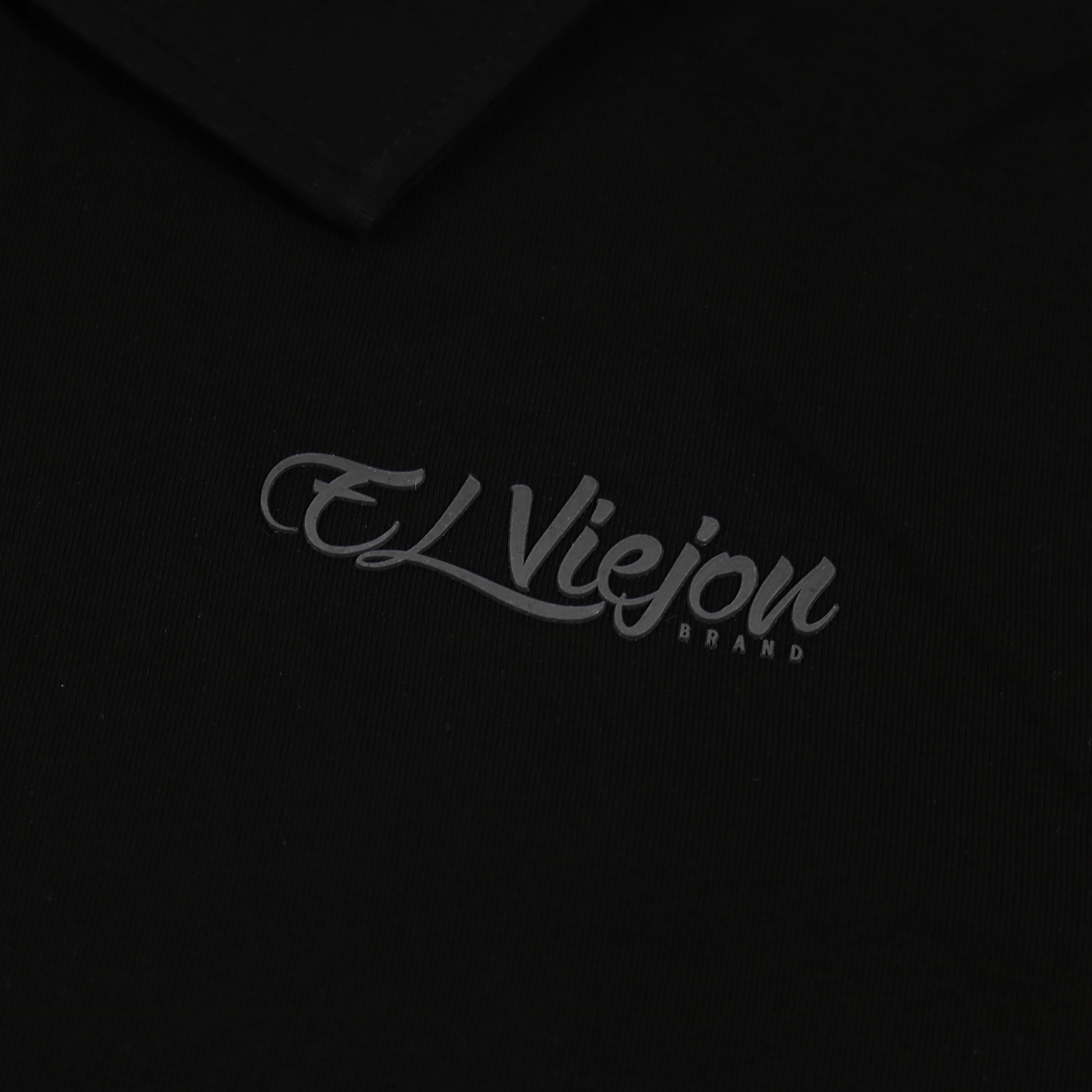 Black polo shirt with a subtle charcoal 3D vinyl "El Viejon Brand" logo.
