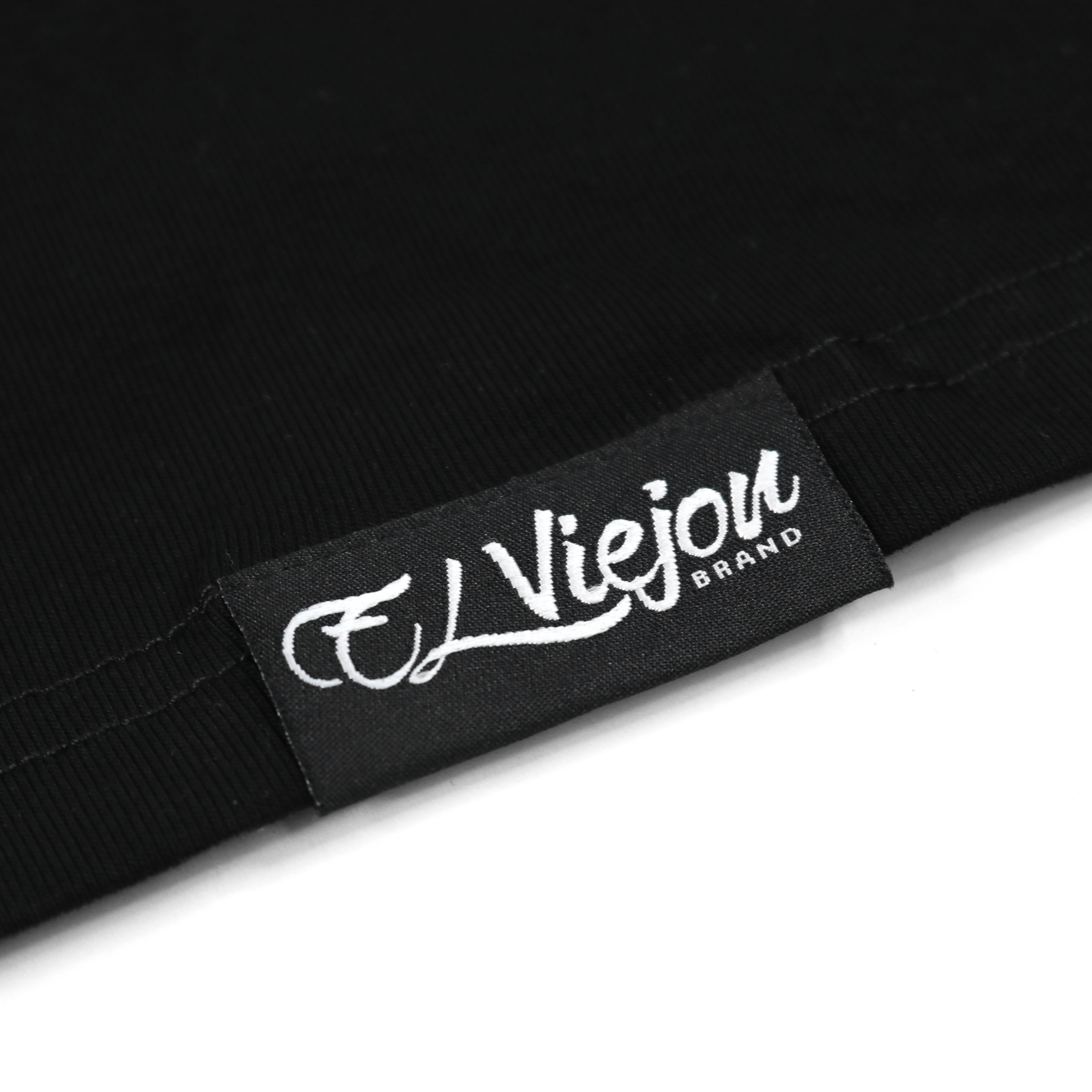 Close-up of a black polo shirt fabric with a woven black "El Viejon Brand" label in white script.