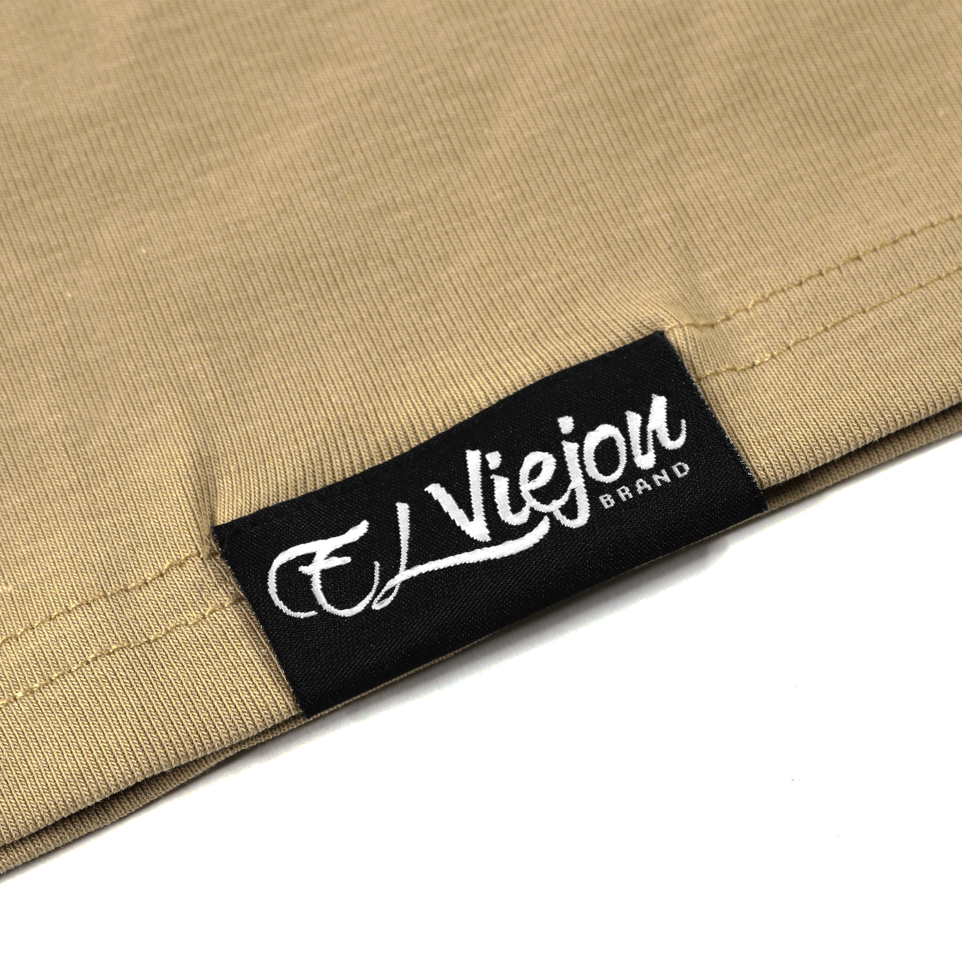 Close-up of a sand-colored polo shirt with a black "El Viejon Brand" woven label.