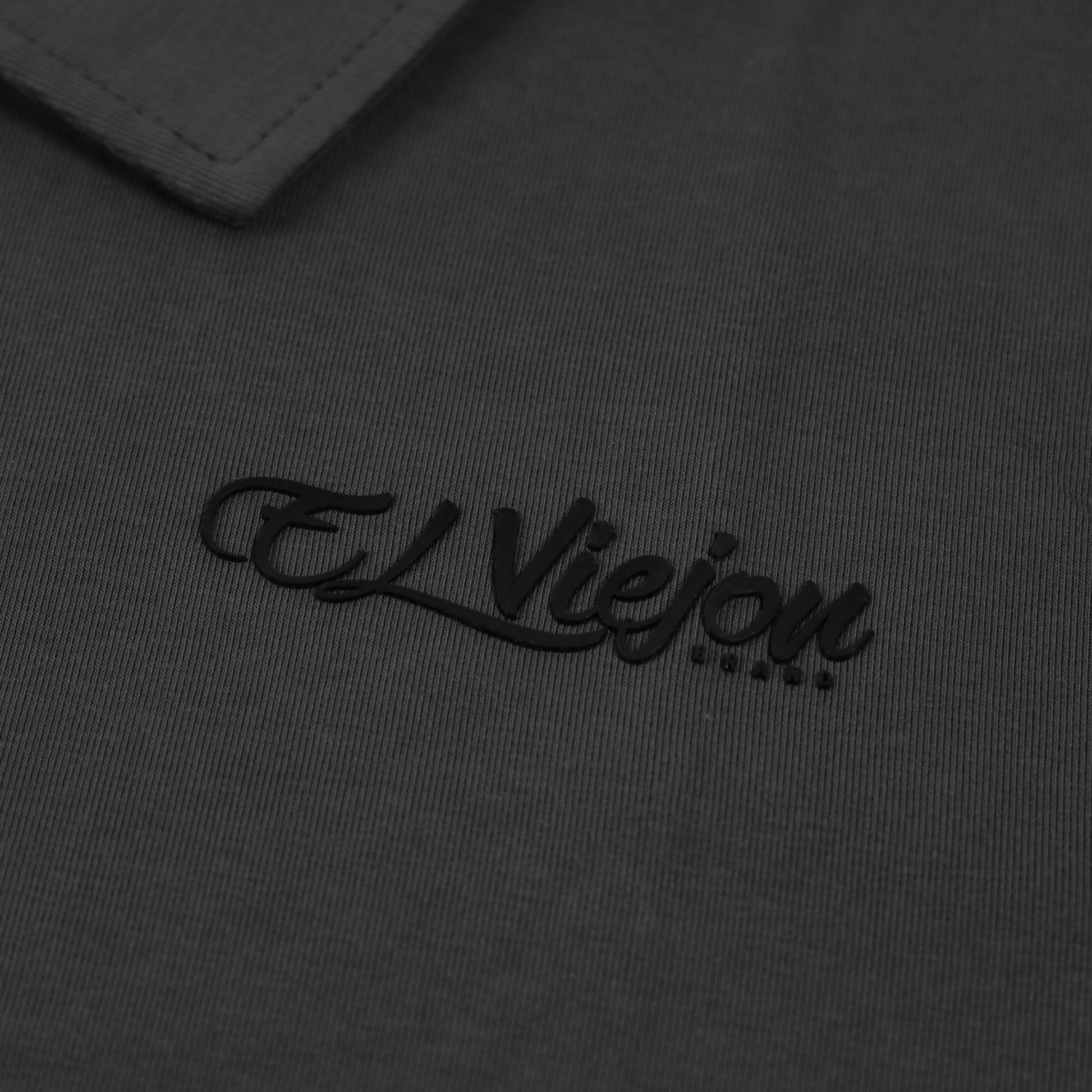 Charcoal polo shirt with a black 3D vinyl "El Viejon Brand" logo and a ribbed texture.