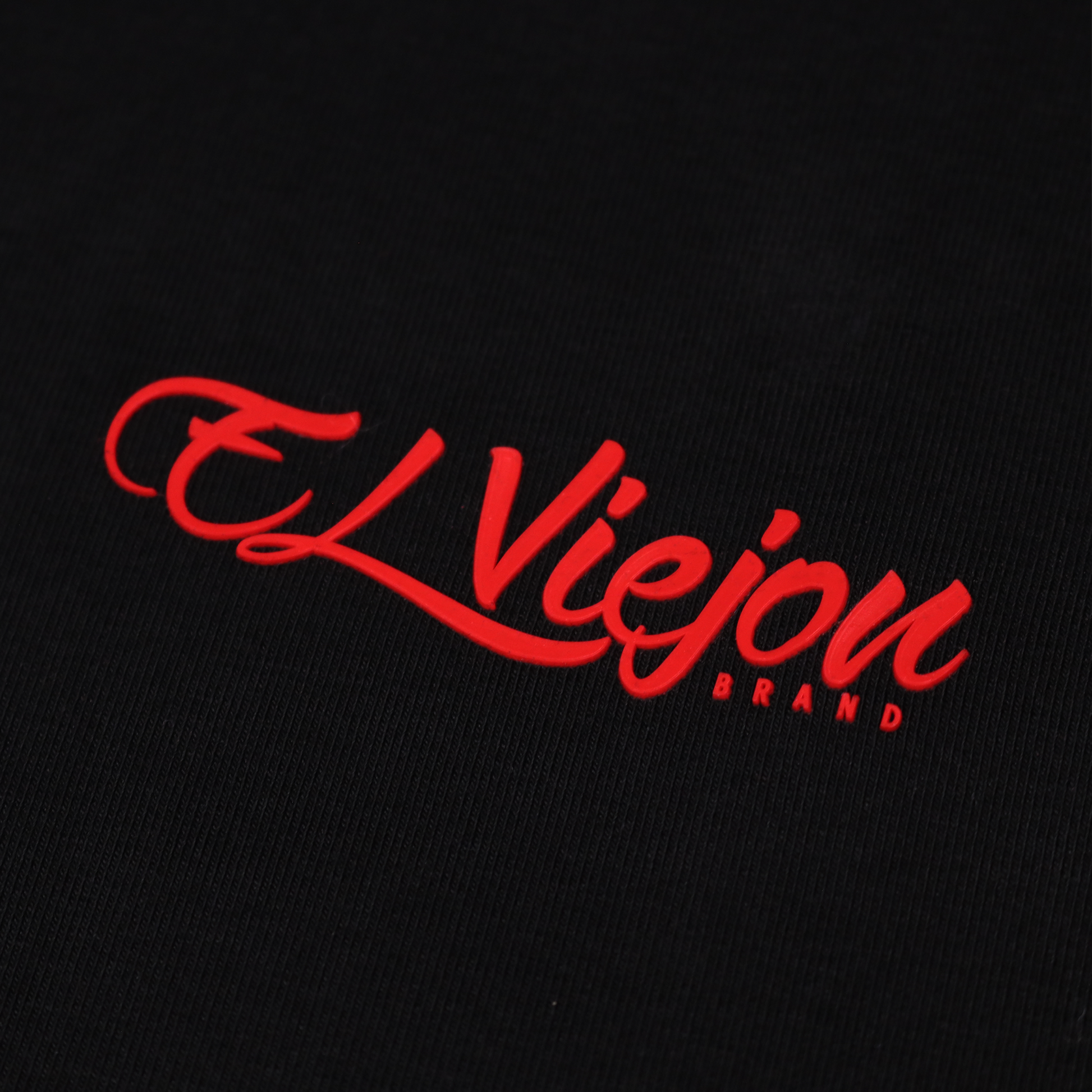 Close-up of a black polo shirt with a raised red "El Viejon Brand" 3D vinyl logo.