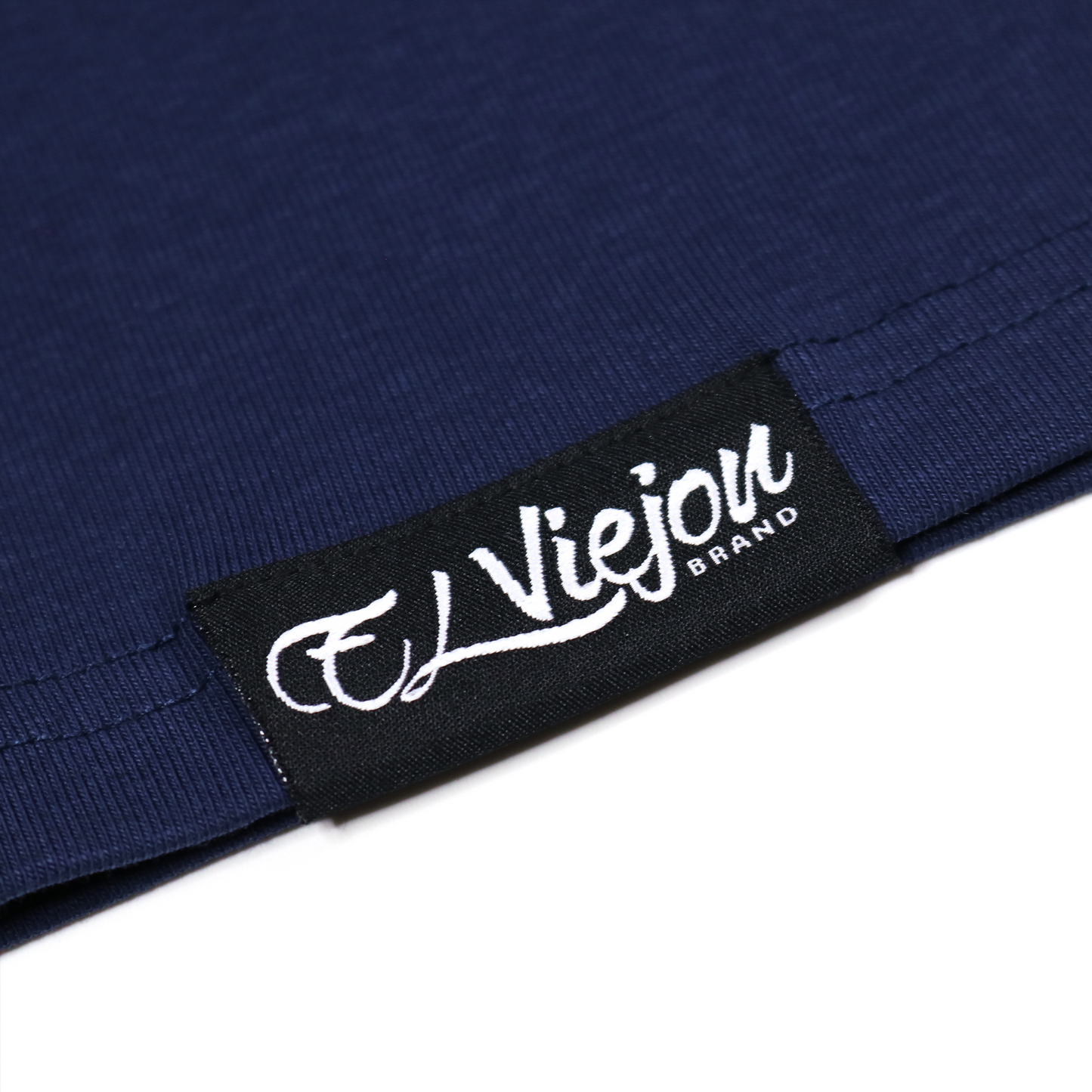 Close-up of a navy blue polo shirt with a black "El Viejon Brand" tag featuring white lettering.