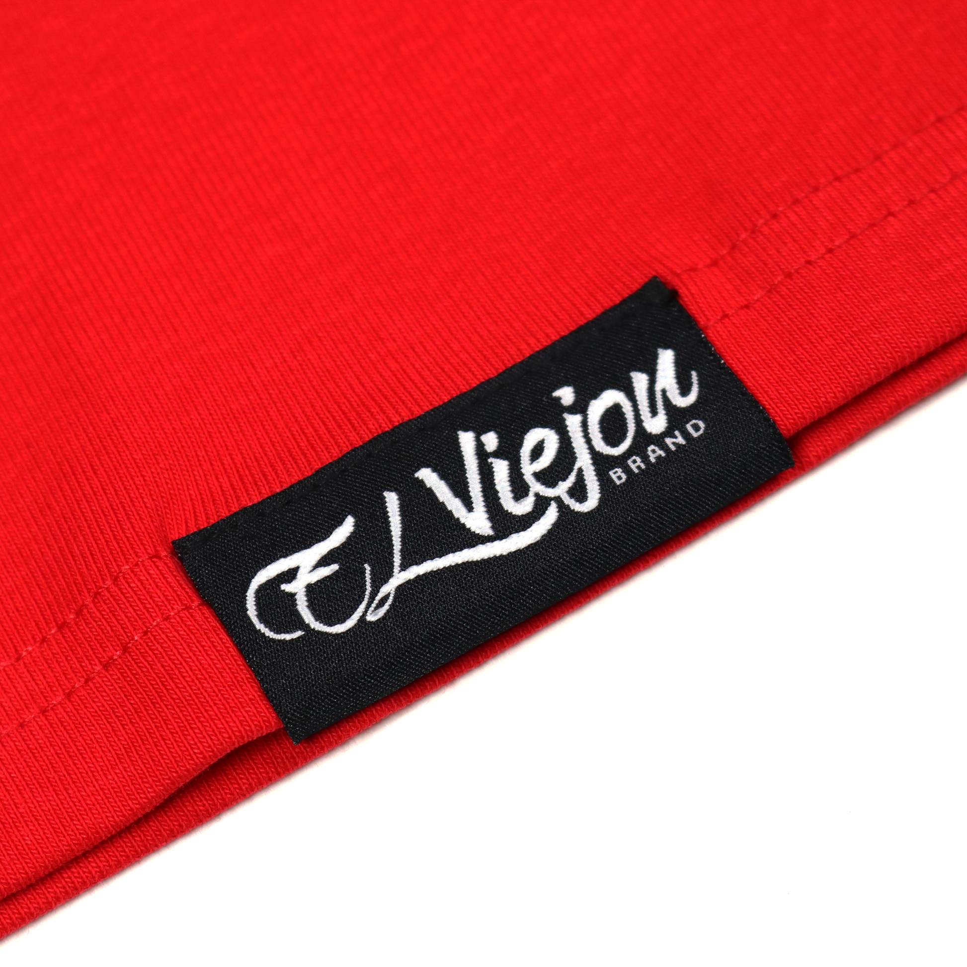 Close-up of a red polo shirt with a black woven label featuring the white "El Viejon Brand" logo.
