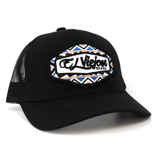 Black TruCap trucker hat with mesh back, pre-curved visor, and "El Viejou Brand" patch with geometric pattern.