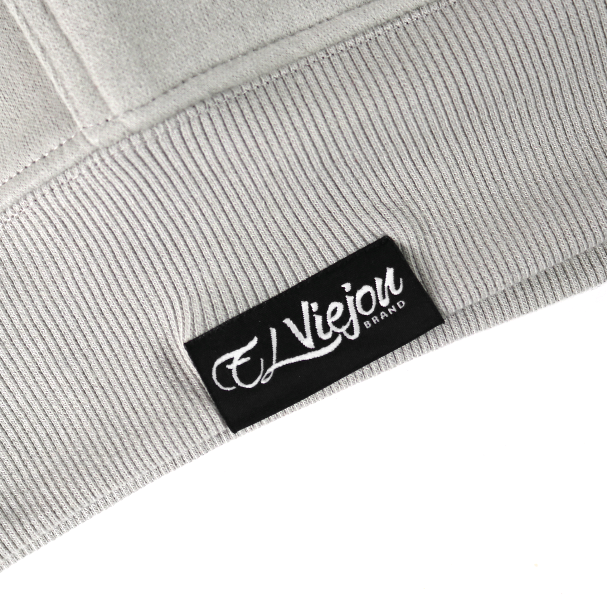 Close-up of the Alpha light grey hoodie's ribbed hem with a black "El Viejou Brand" tag.