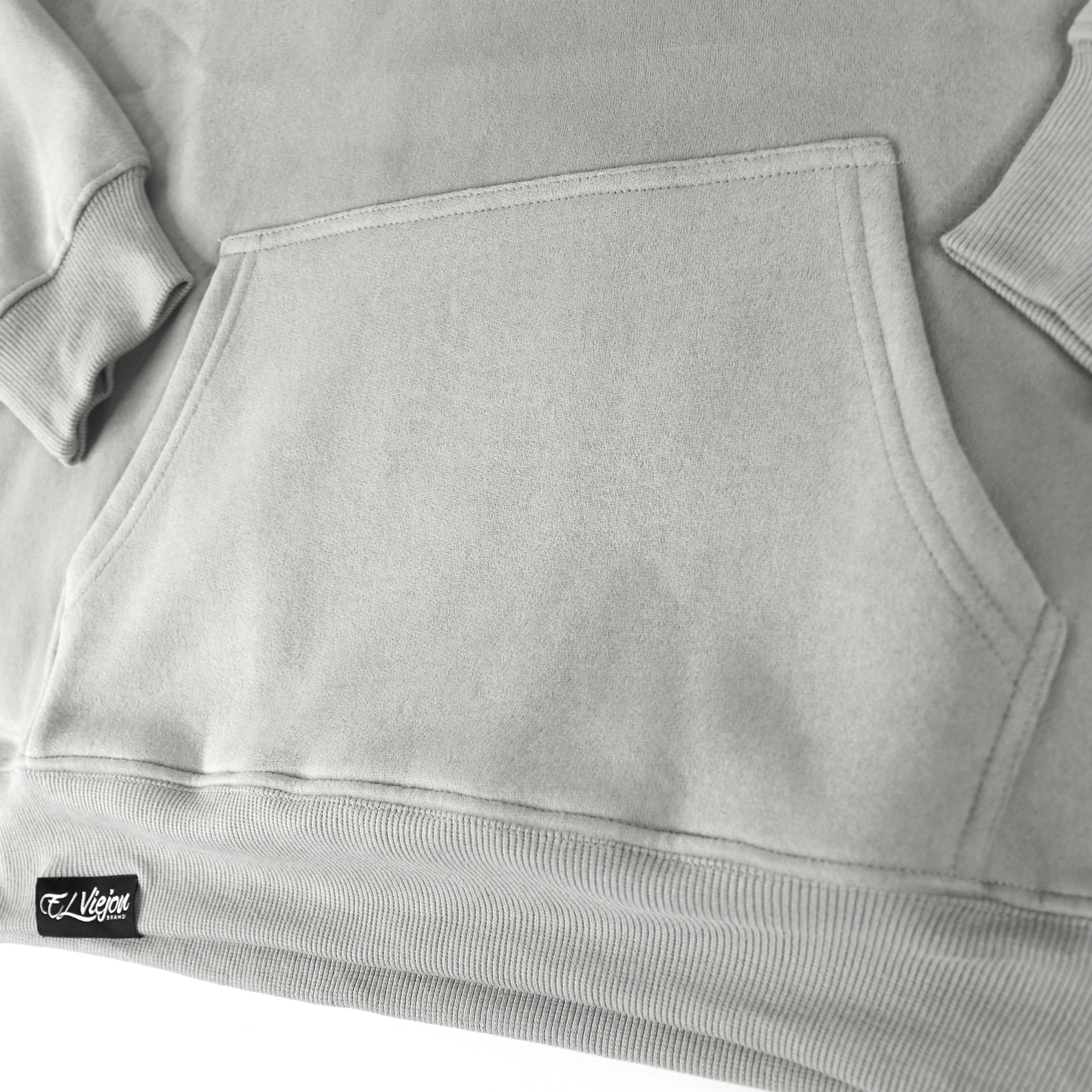 Close-up of Alpha light grey cotton/poly fleece hoodie with front pocket and "El Viejo" woven label.