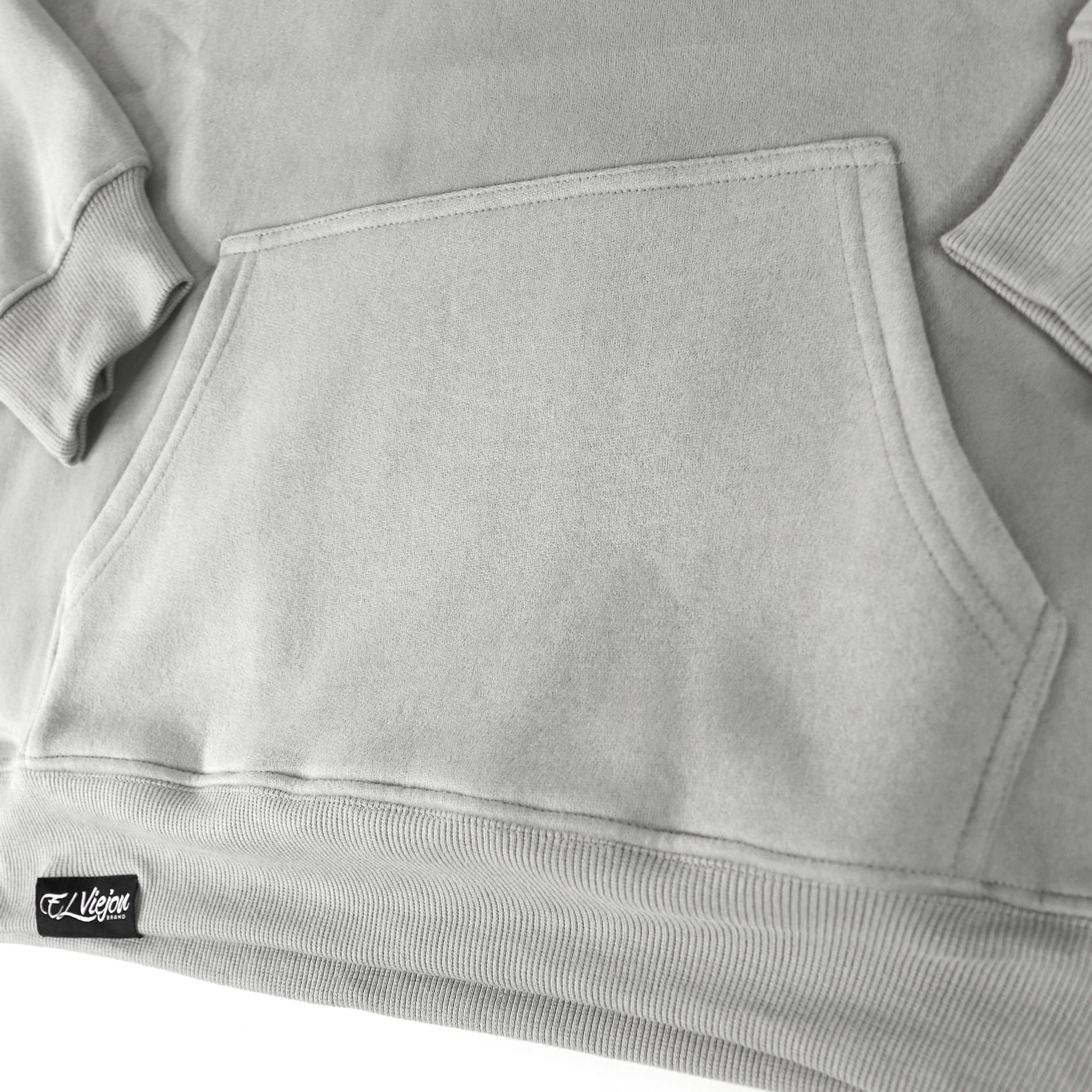 Close-up of Alpha light grey cotton/poly fleece hoodie with front pocket and "El Viejo" woven label.
