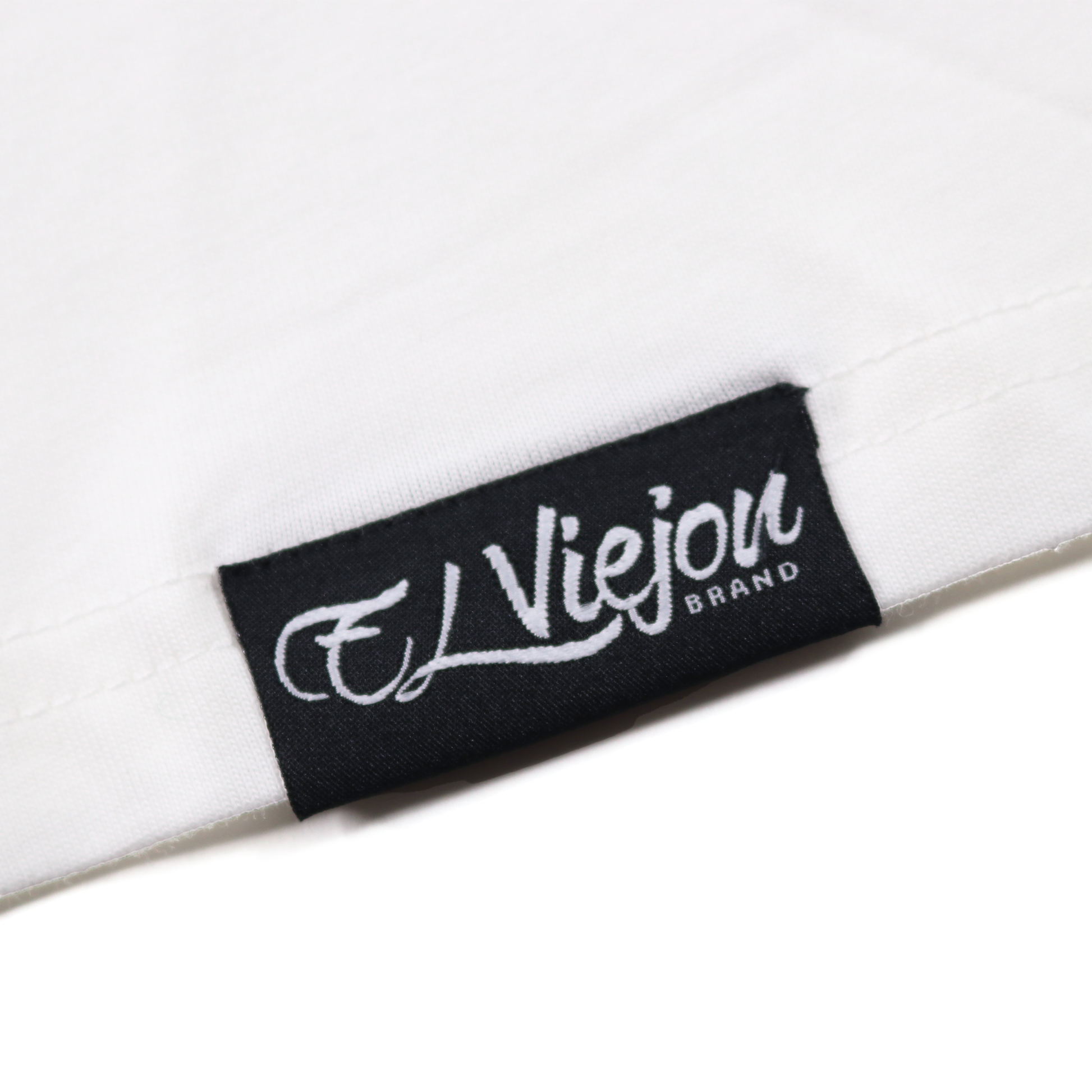 Close-up of a white cotton Alpha shirt with a black woven "El Viejon Brand" label.