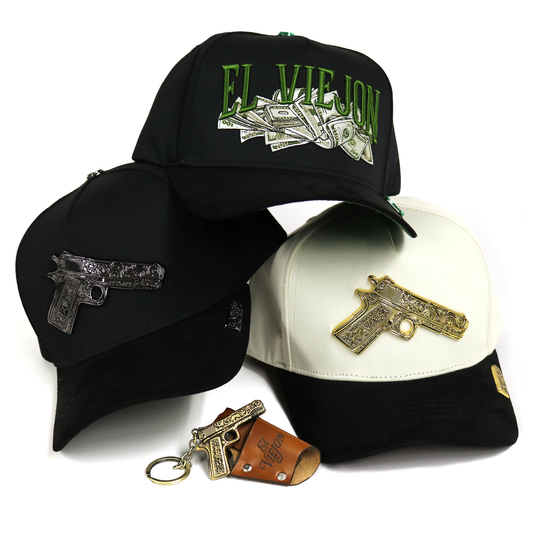 Three black baseball caps with gun-shaped metal embellishments and a matching keychain, shown on a white background. One cap has green 'EL VIEJO' text with money graphics, one is black with a silver gun emblem, and one is black and white with a gold gun emblem.
