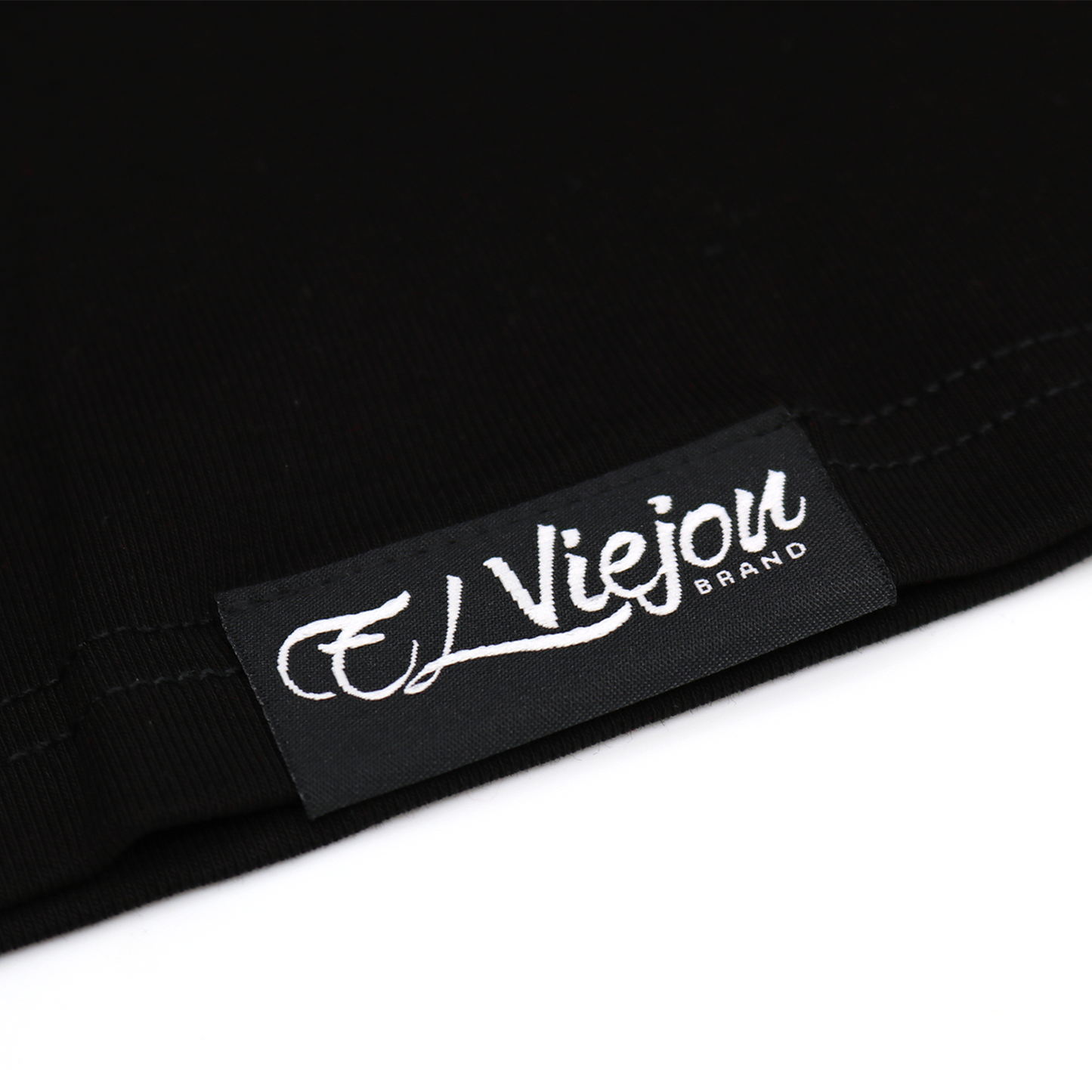 Close-up of a black fabric tag with "El Viejon Brand" in white script on a black polo shirt.
