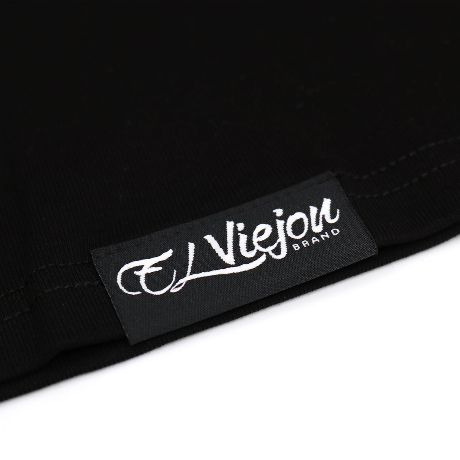 Close-up of a black fabric tag with "El Viejon Brand" in white script on a black polo shirt.