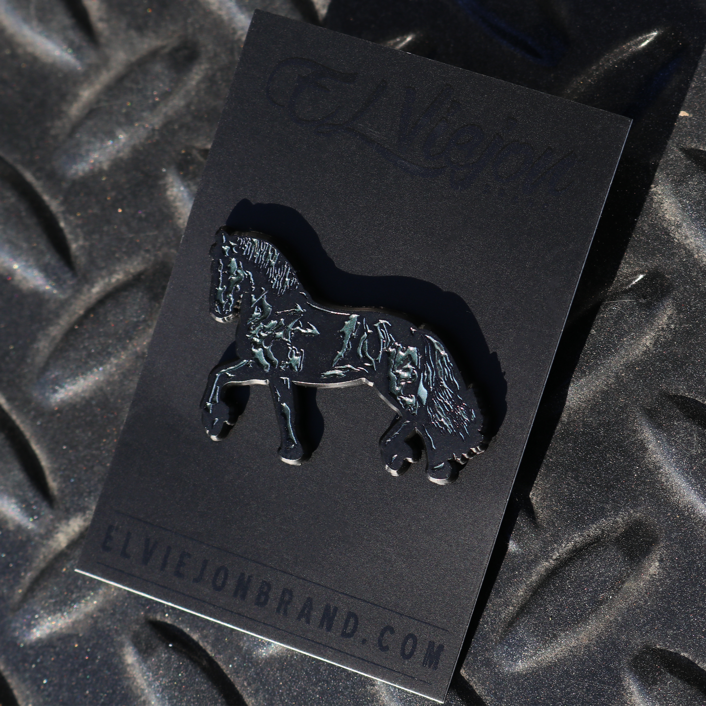 Black enamel Frison horse pin with iridescent details on a black backing card.