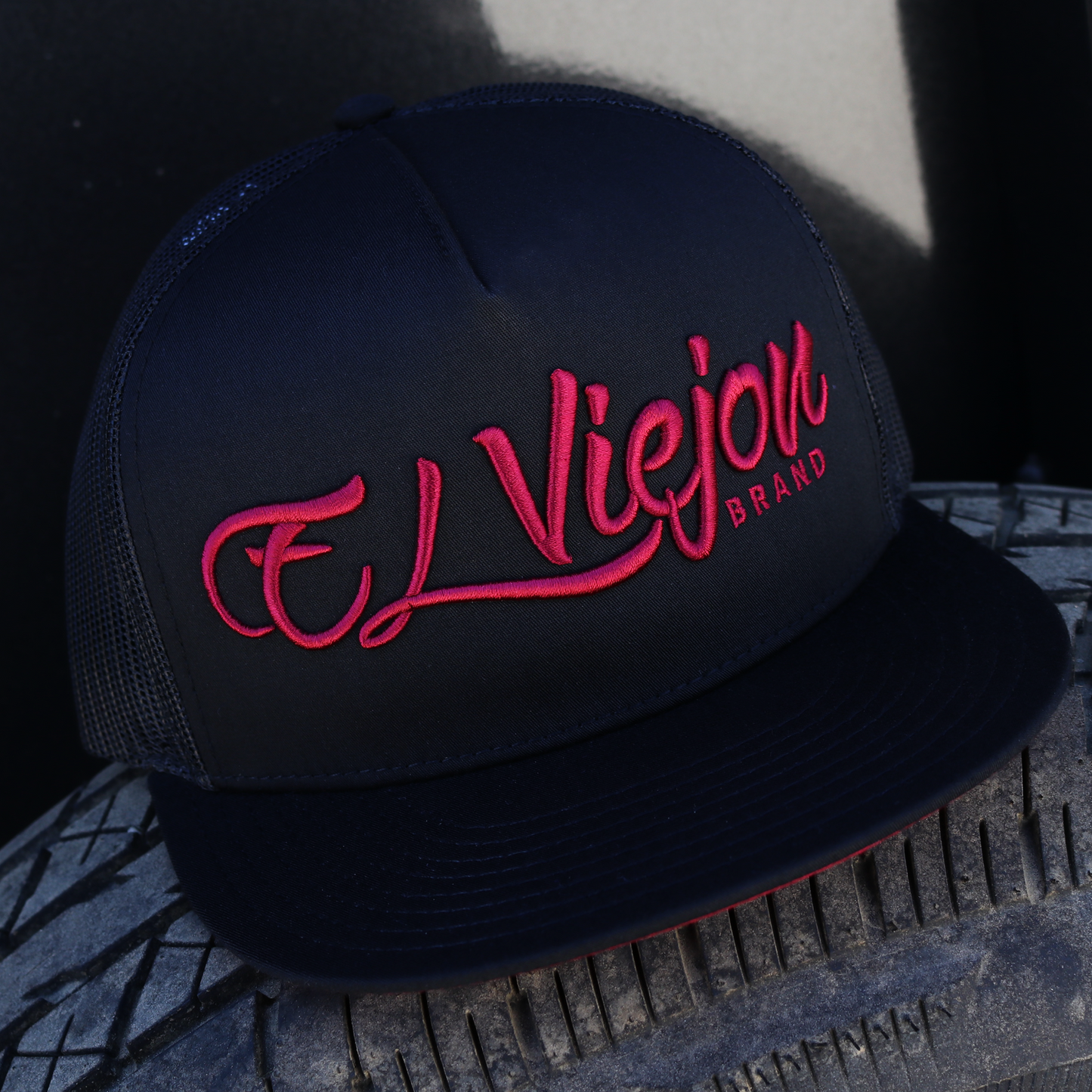 Black flat visor hat with "El Viejon Brand" in red script, black mesh back, and adjustable snapback.