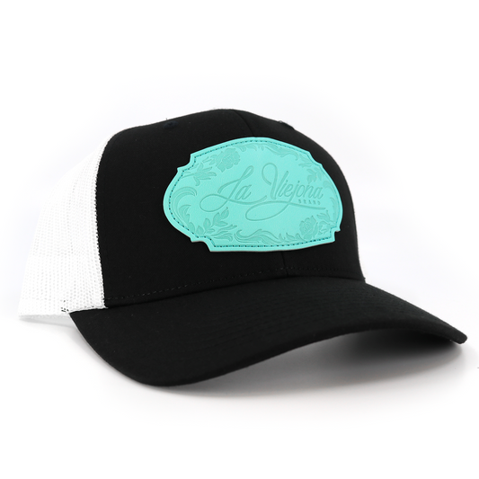 La Viejona Floral Black/White TruCap™ trucker hat with a turquoise floral patch.