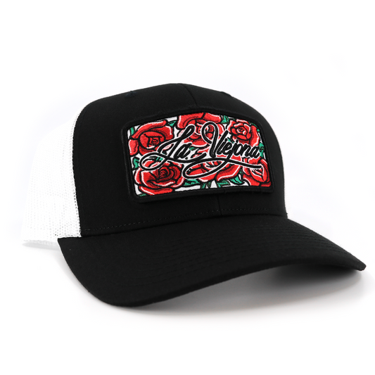 Black and white trucker hat with a "La Vieja" red rose embroidered patch.