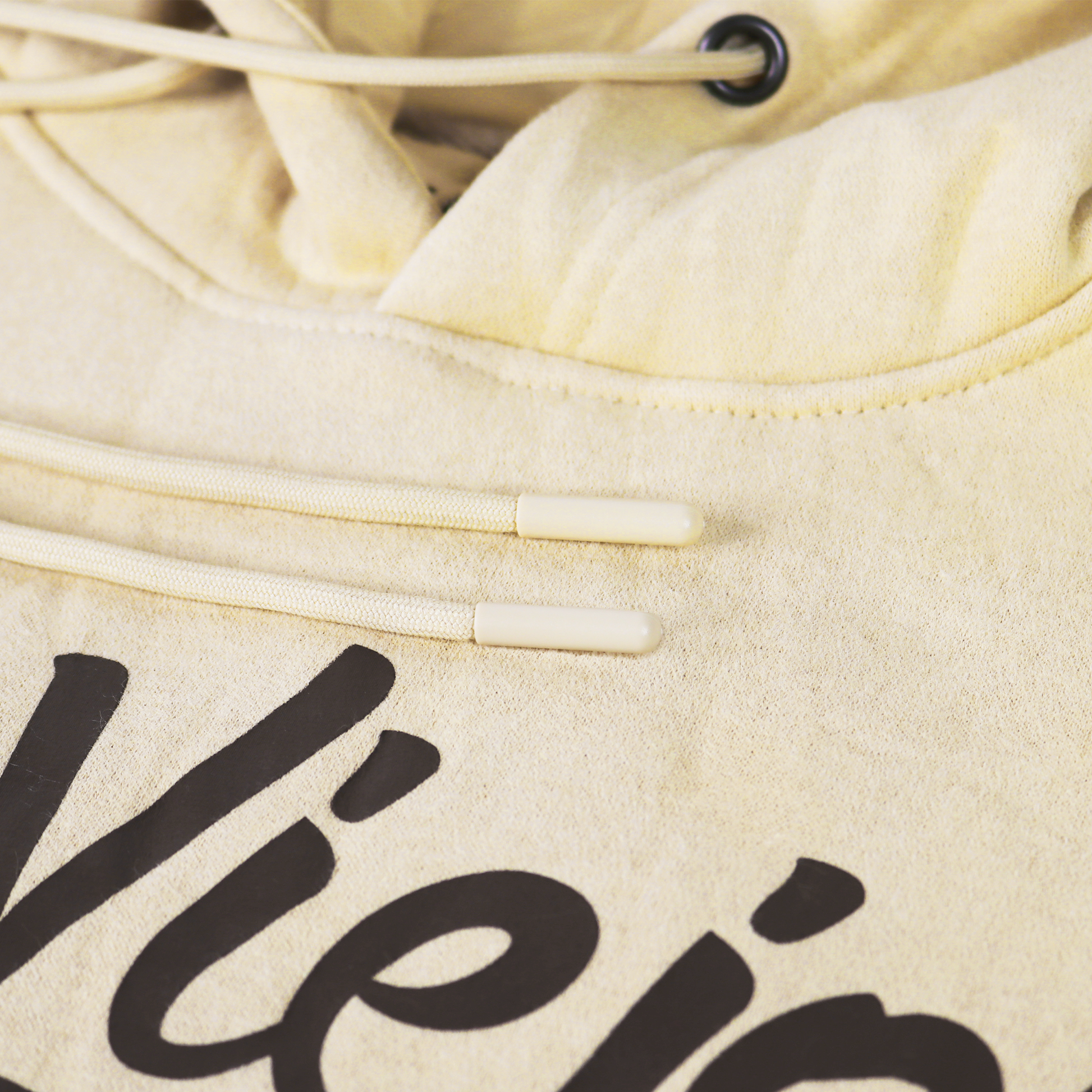 Close-up of a sand-colored cotton/poly fleece hoodie with black screen-printed logo and drawstrings.