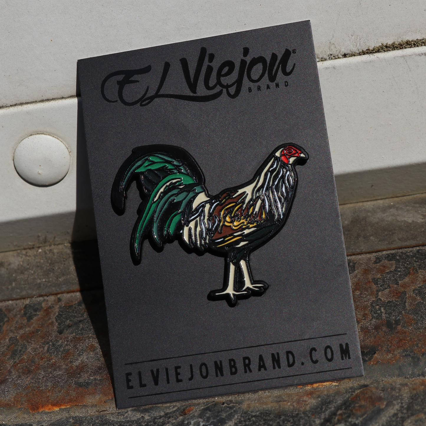 Gallo Giro enamel pin on black card, featuring a colorful rooster with green tail feathers.