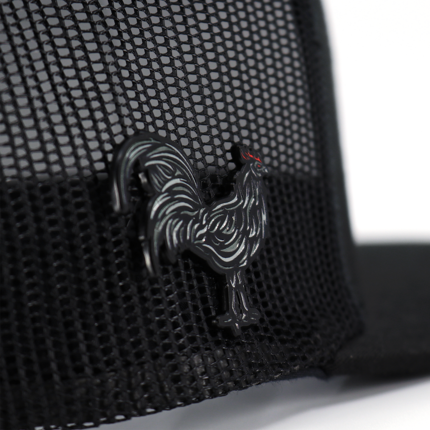Black Gallo Negro enamel pin with red comb, attached to a black mesh hat.