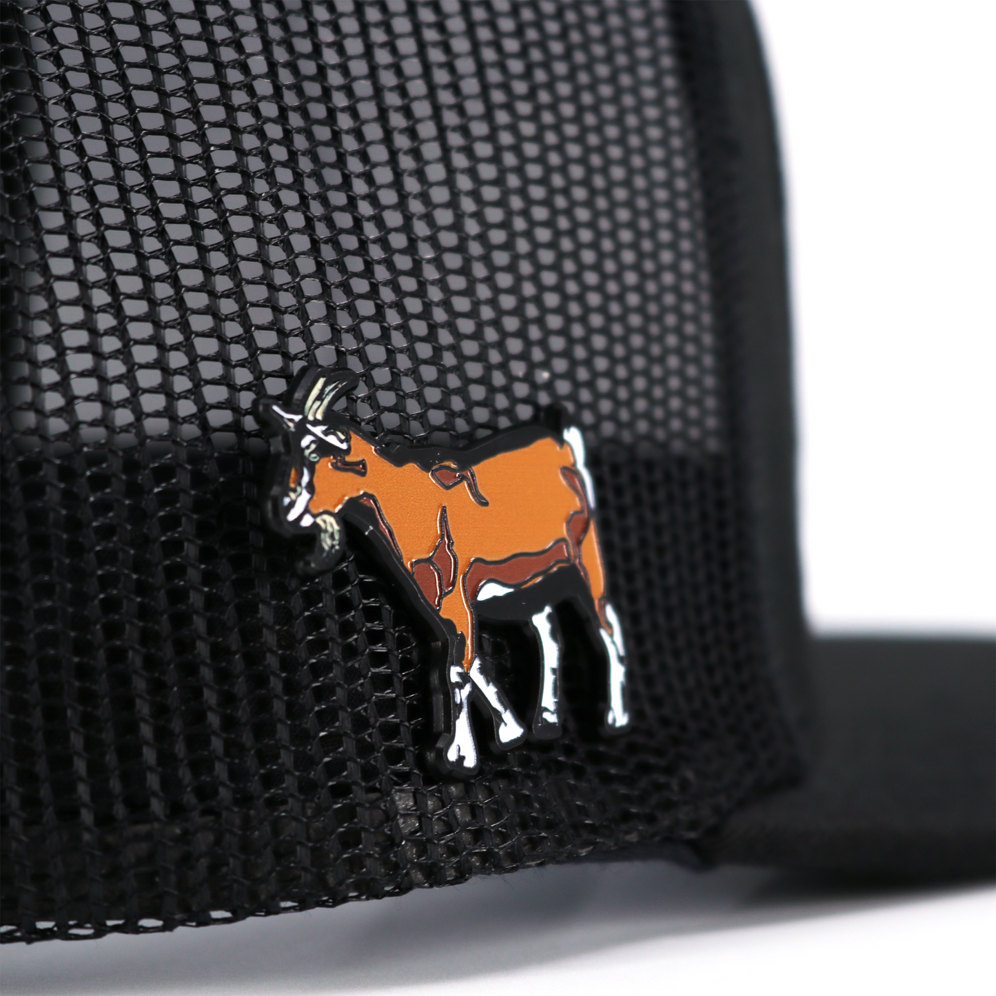 Chivo Pin: Brown and white goat enamel pin with black outline, attached to a black mesh hat.