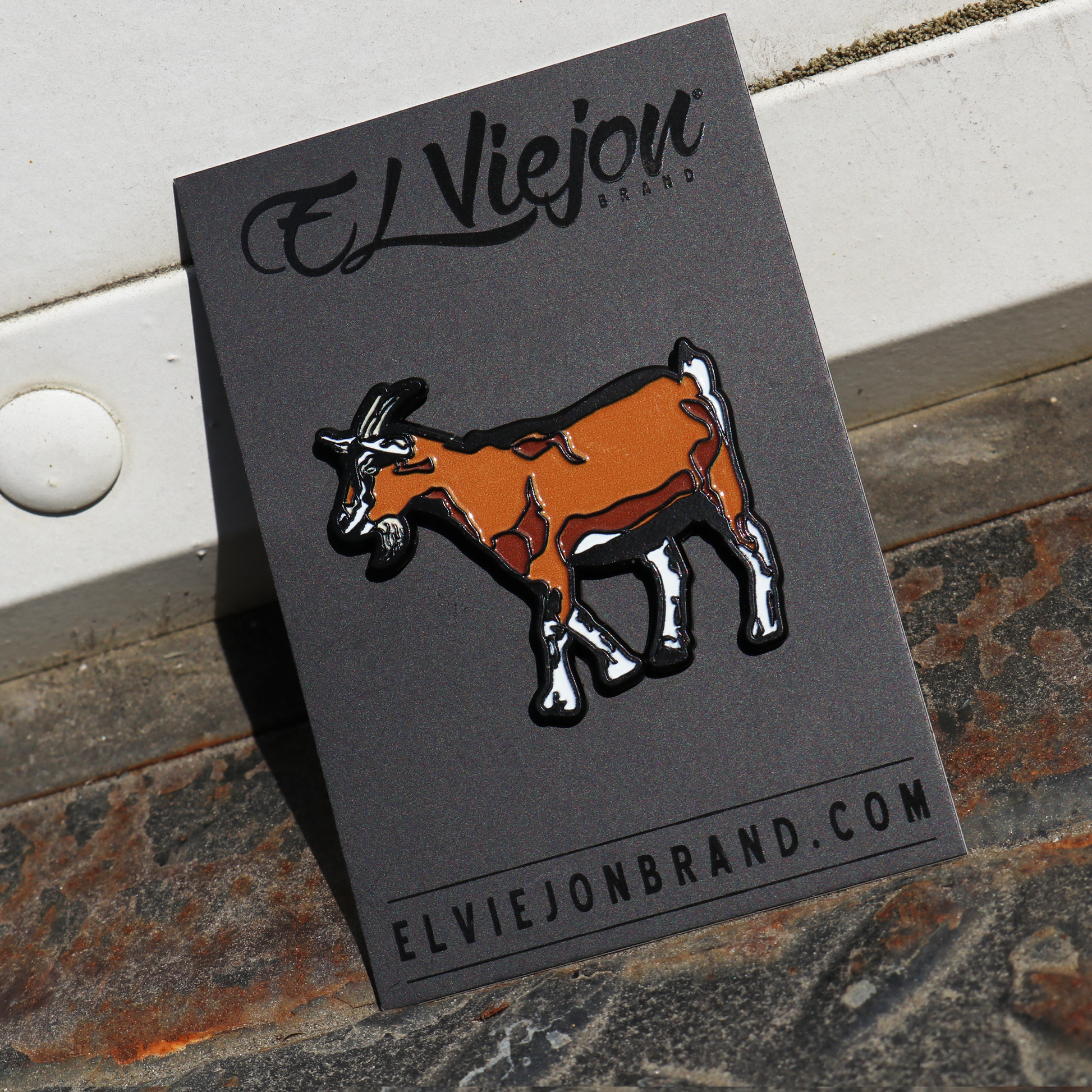 El Chivo Pin, brown and white goat enamel pin on black El Viejon Brand card.