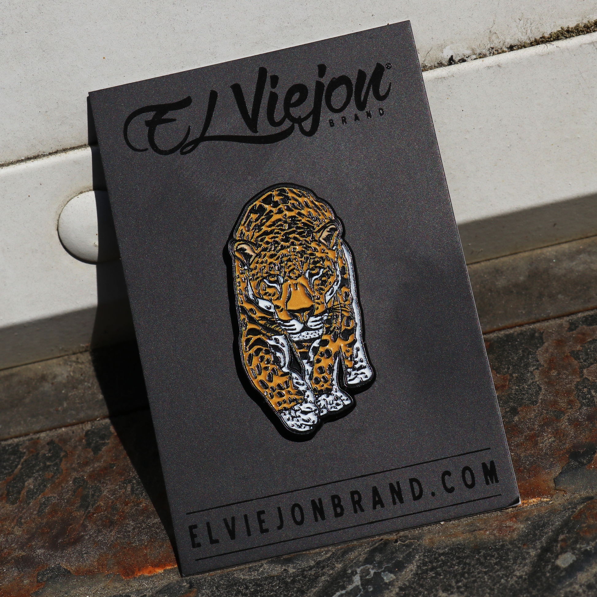 Jaguar enamel pin with black outlines, orange and white spots, on a black El Viejon Brand card.