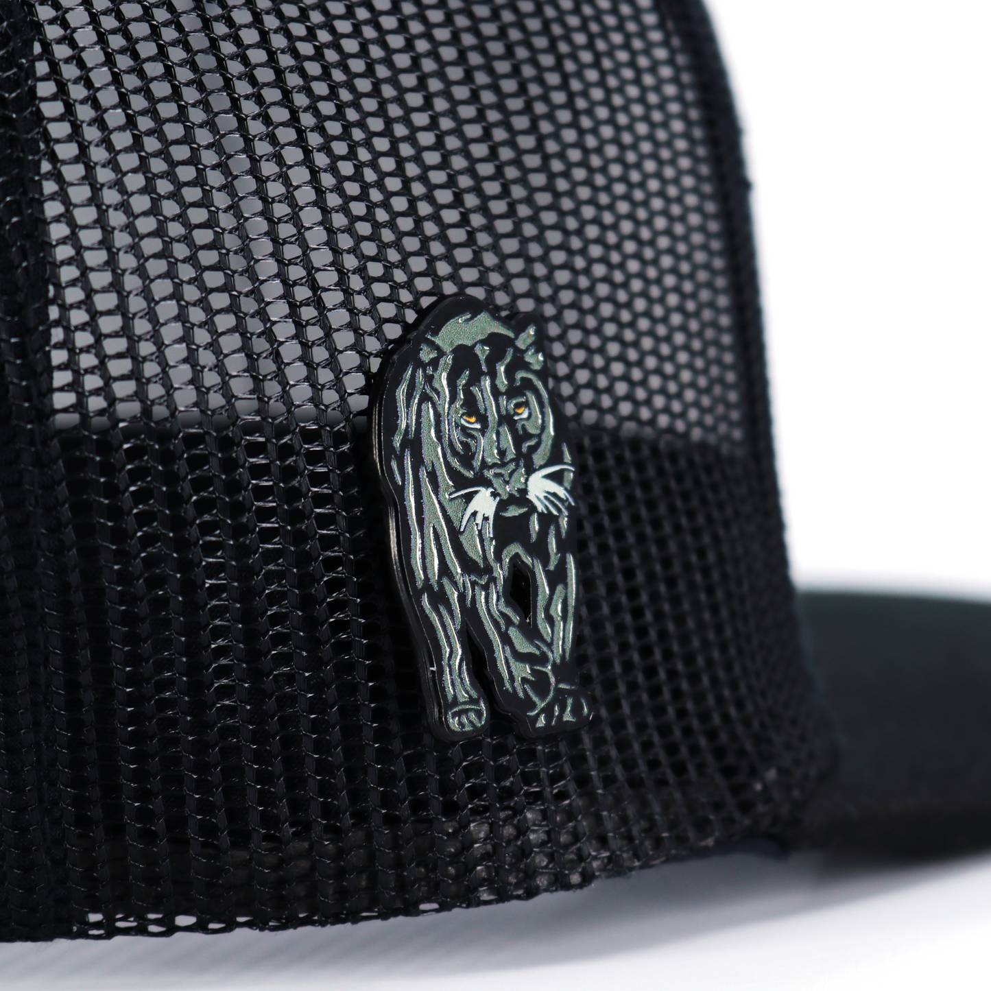 Black Pantera Negra enamel pin with yellow eyes, attached to a black mesh cap.