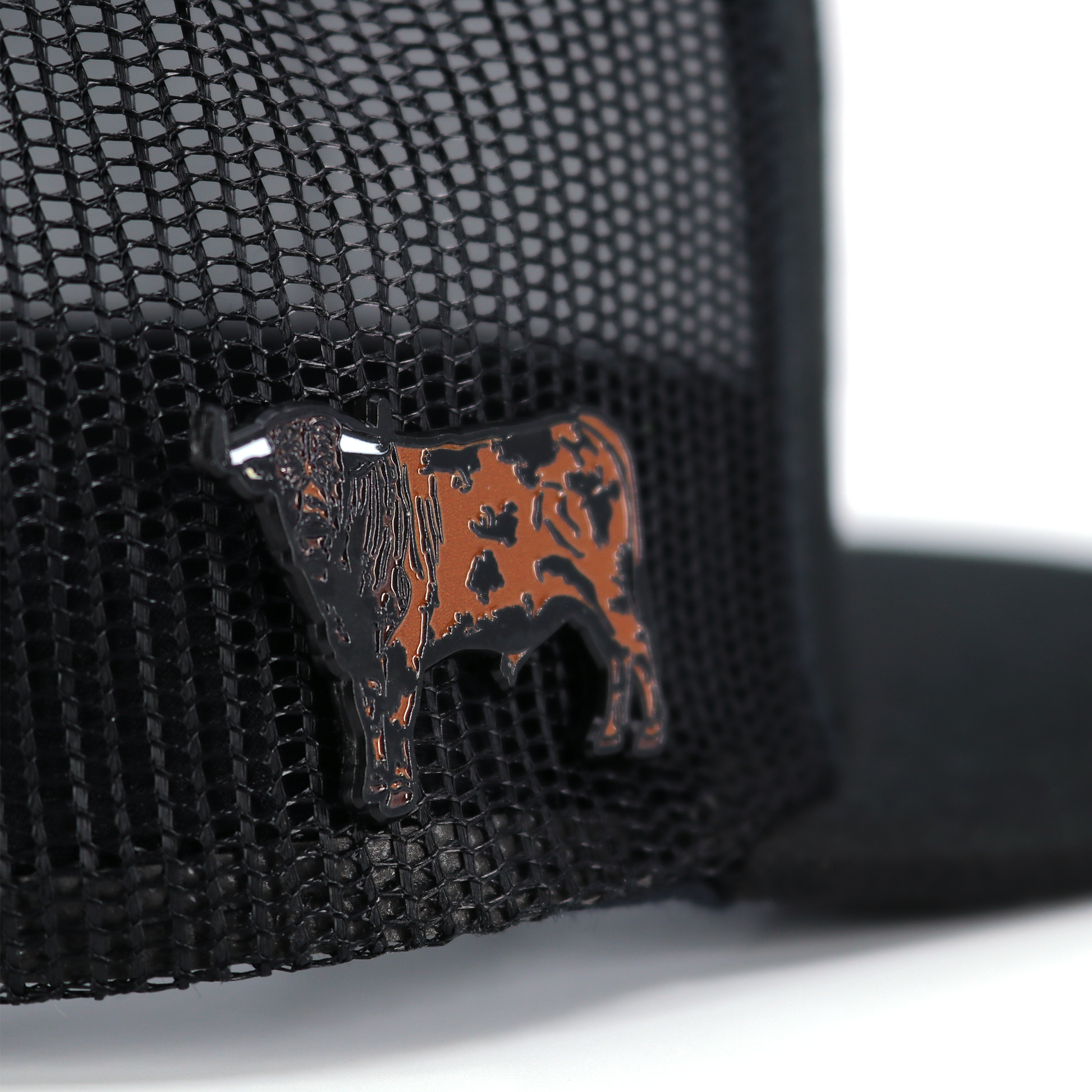 Semental Pin de metal esmaltado negro y cobre con diseño de toro, sobre gorra de malla negra.