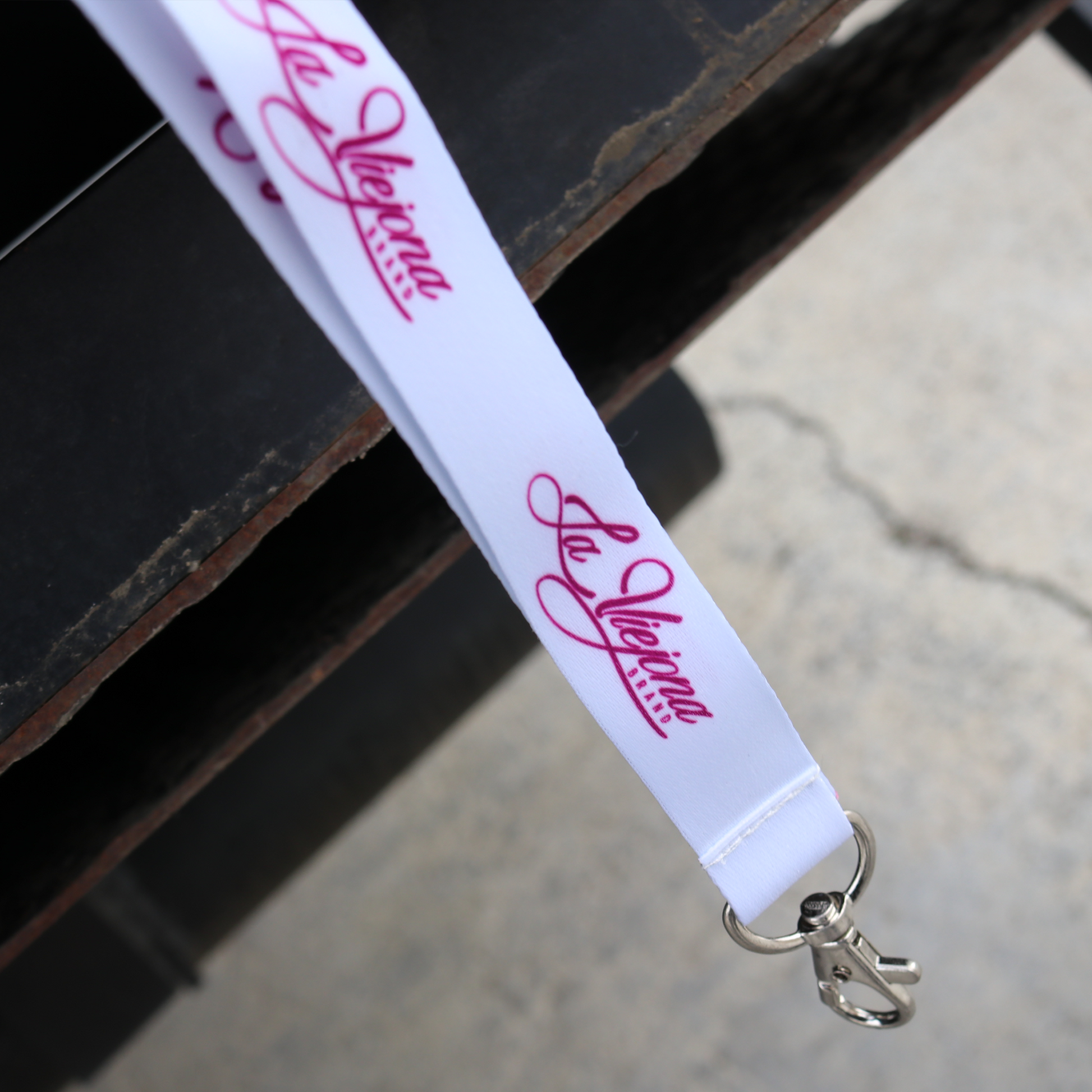 White La Viejona brand lanyard with repeating pink script logo and silver metal swivel clip.
