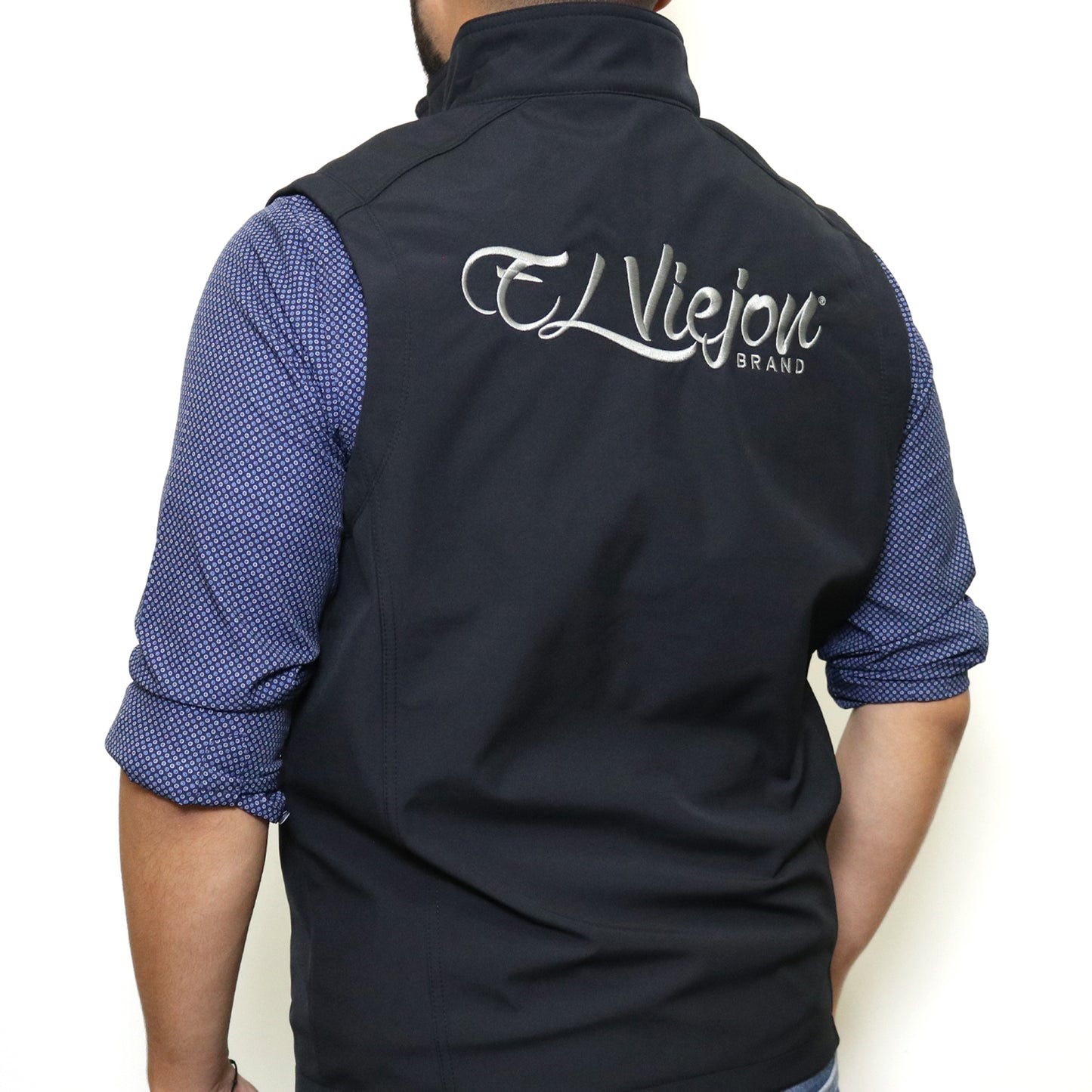 Black El Viejon Brand Vest, back view, with charcoal embroidered logo, worn over a blue patterned shirt.