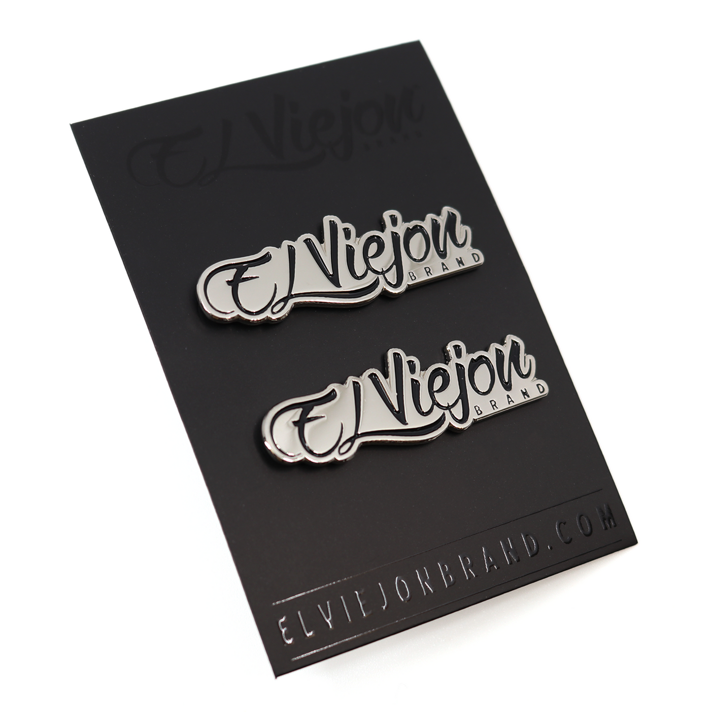 Two shiny silver El Viejon Brand pins on a black card.