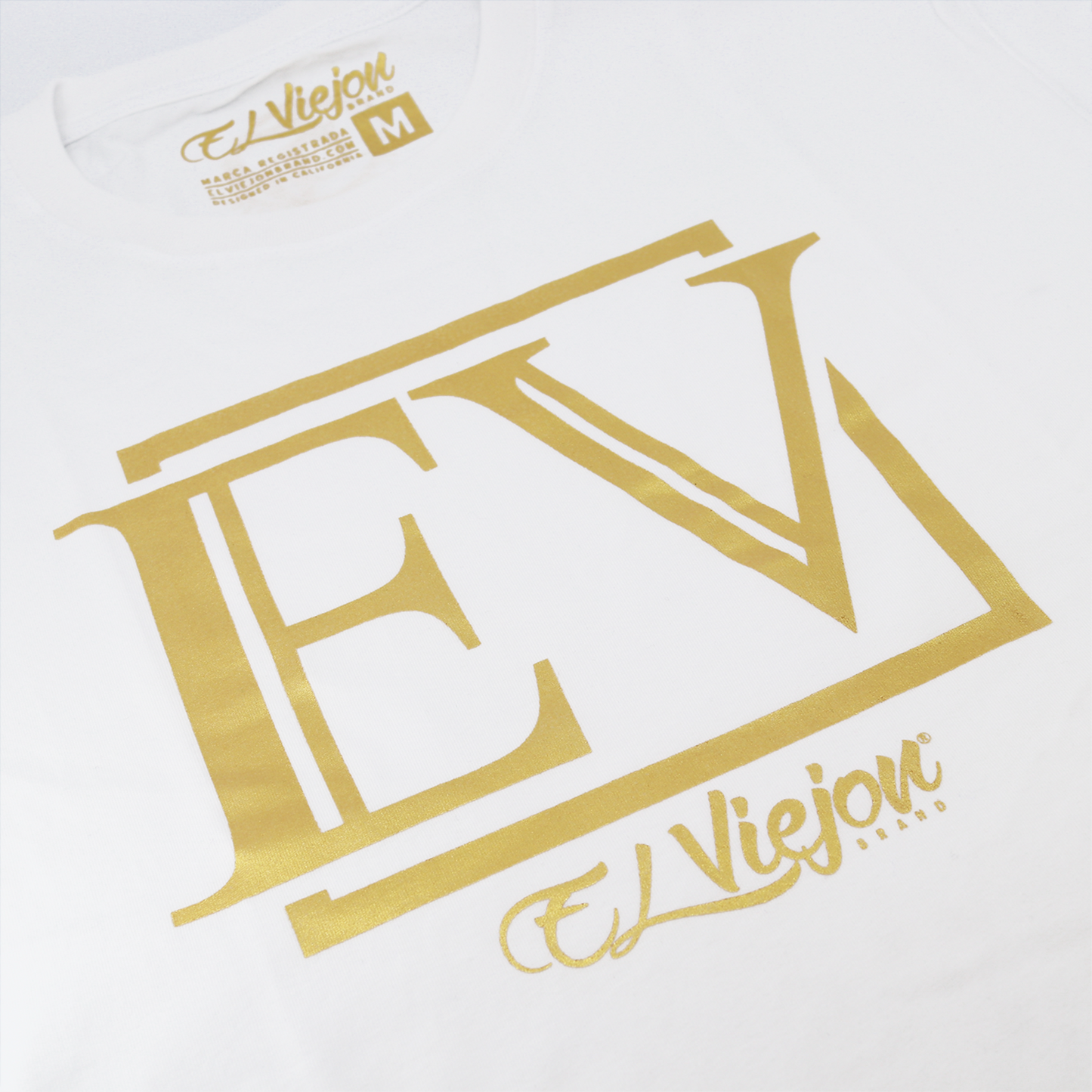 White 100% cotton Eminencia shirt with large gold "EV" logo and "El Viejon Brand" script.