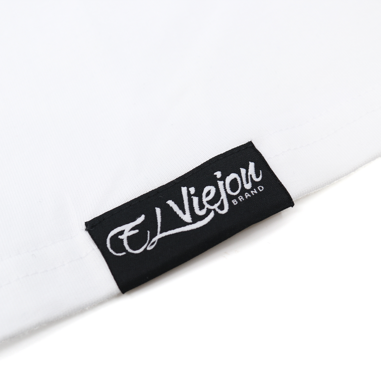 Close-up of a white Eminencia cotton shirt with a black "El Viejon Brand" woven label.