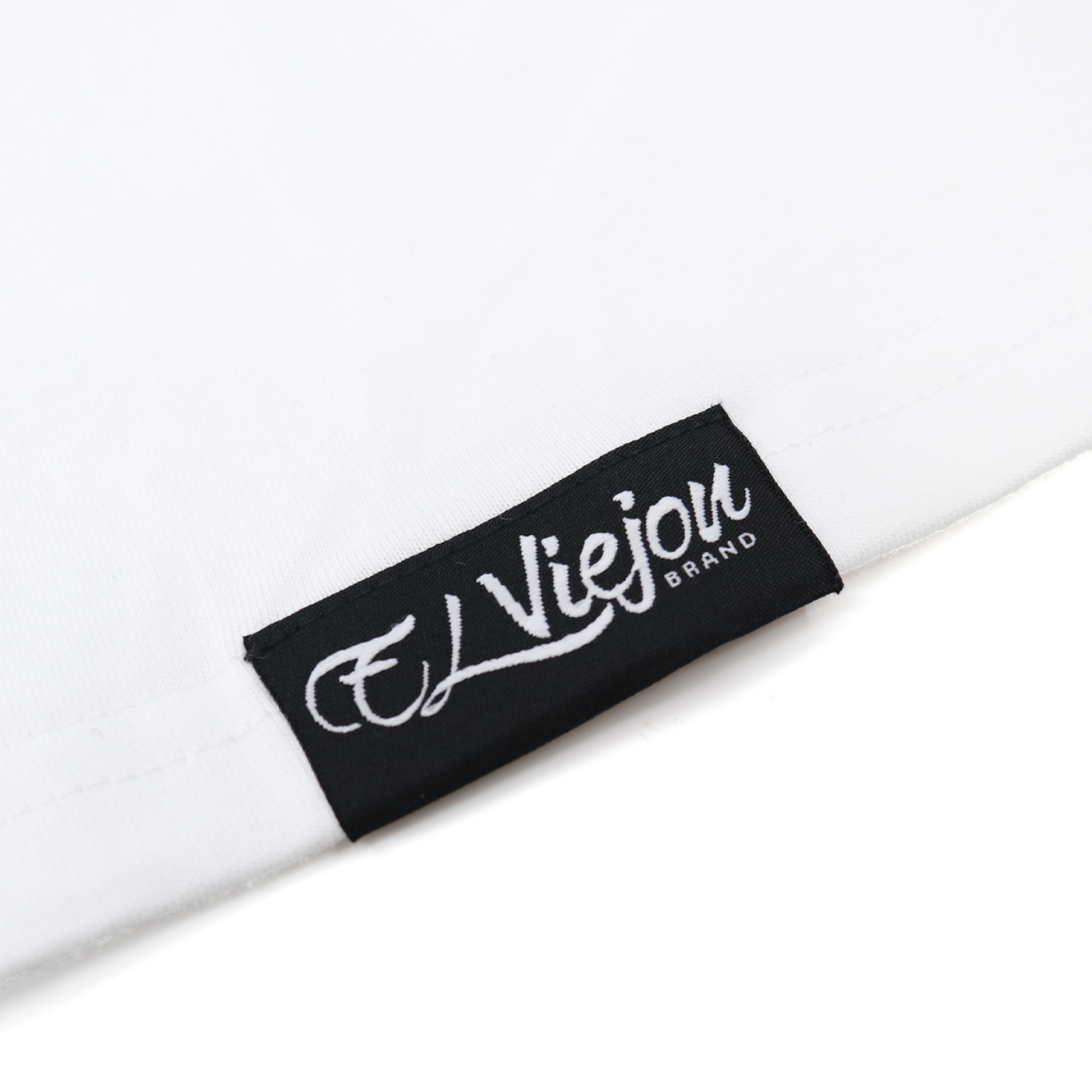 Close-up of a white Eminencia cotton shirt with a black "El Viejon Brand" woven label.