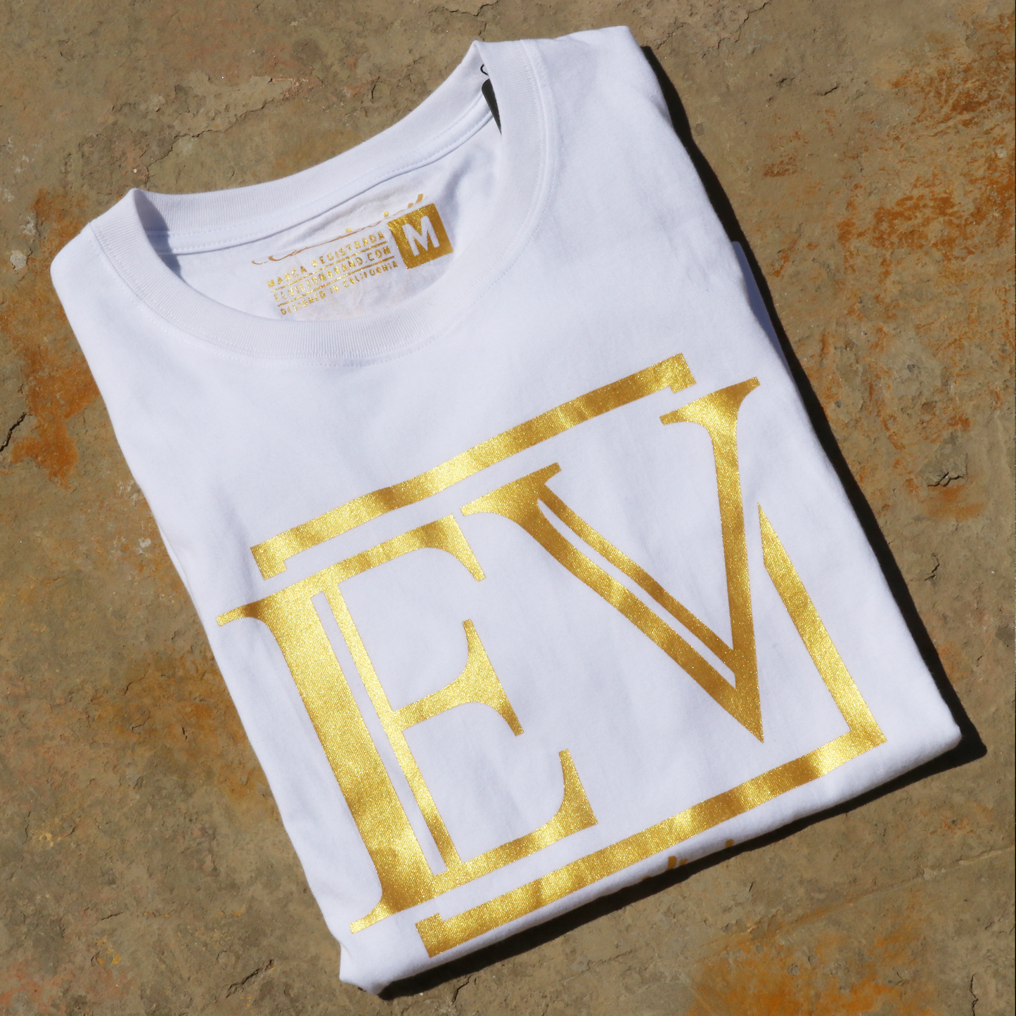 White Eminencia 100% cotton shirt, folded, with a large gold "EV" logo on the front.
