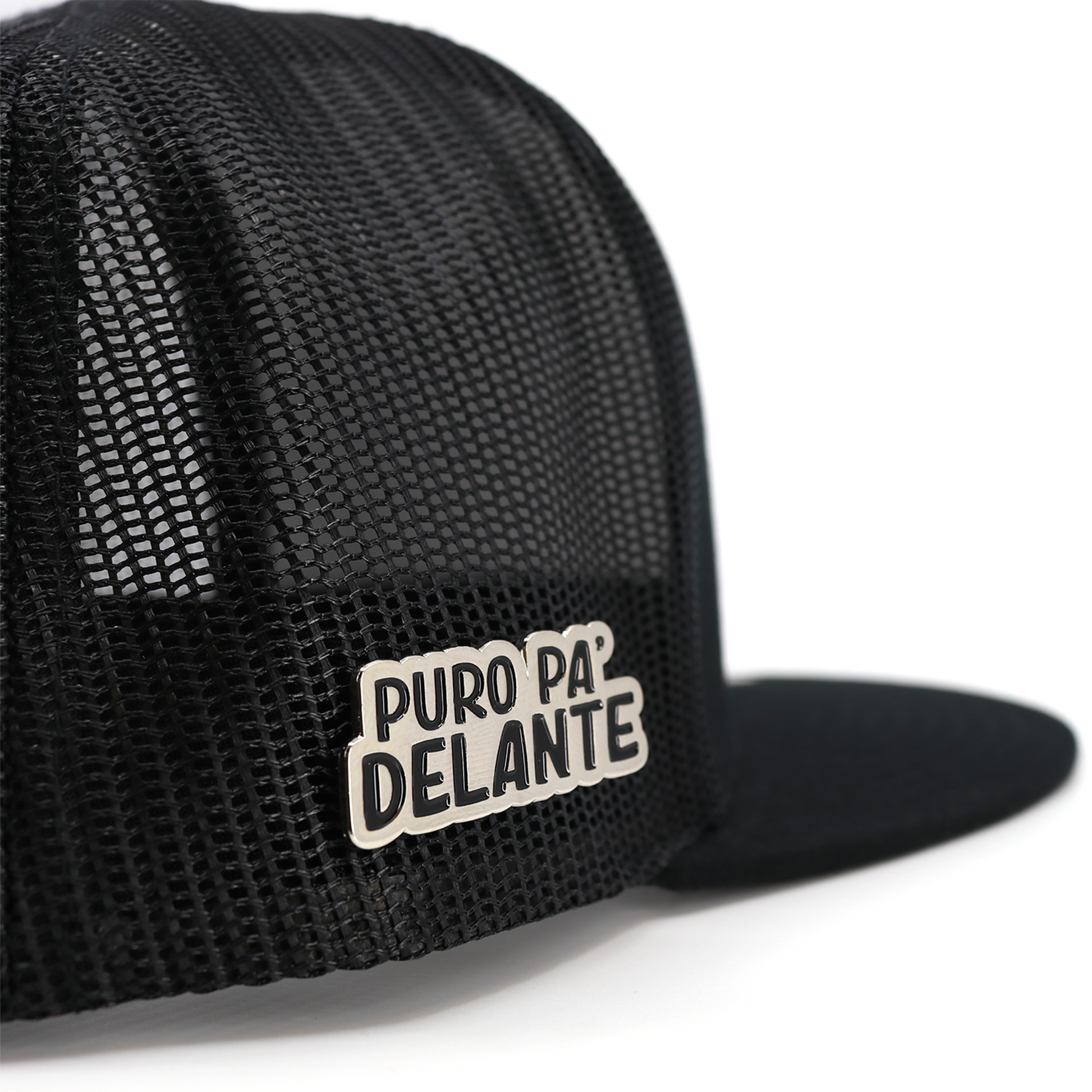 Silver "Puro Pa Delante" pin attached to a black mesh hat.