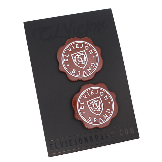 Two round, wavy-edged Sellito Rojo enamel pins with "El Viejon Brand" text on a black card.